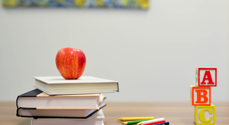 Mesa de colegio con una torre de libros sobre los que hay una manzana